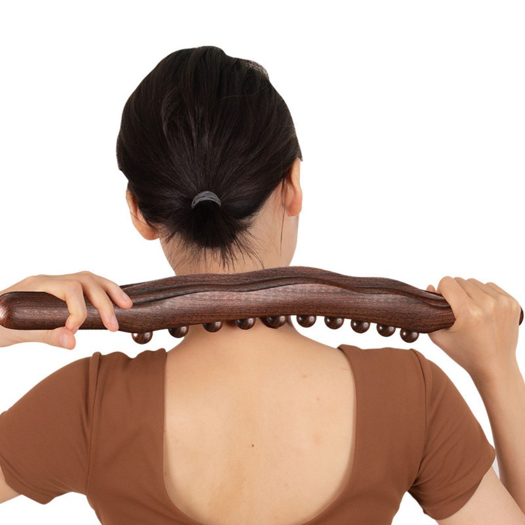 Femme de dos massant sa nuque et ses trapèzes avec le bâton de massage en bois à deux mains
