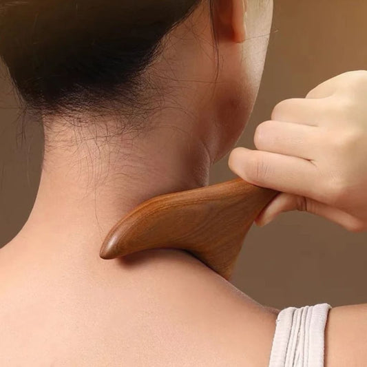 Gros plan d'une femme utilisant l'outil Gua Sha en bois de santal sur un point de pression de la nuque