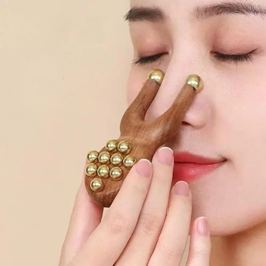 Femme les yeux fermés utilisant le masseur facial en bois sur son front, gros plan sur les billes en laiton dorées